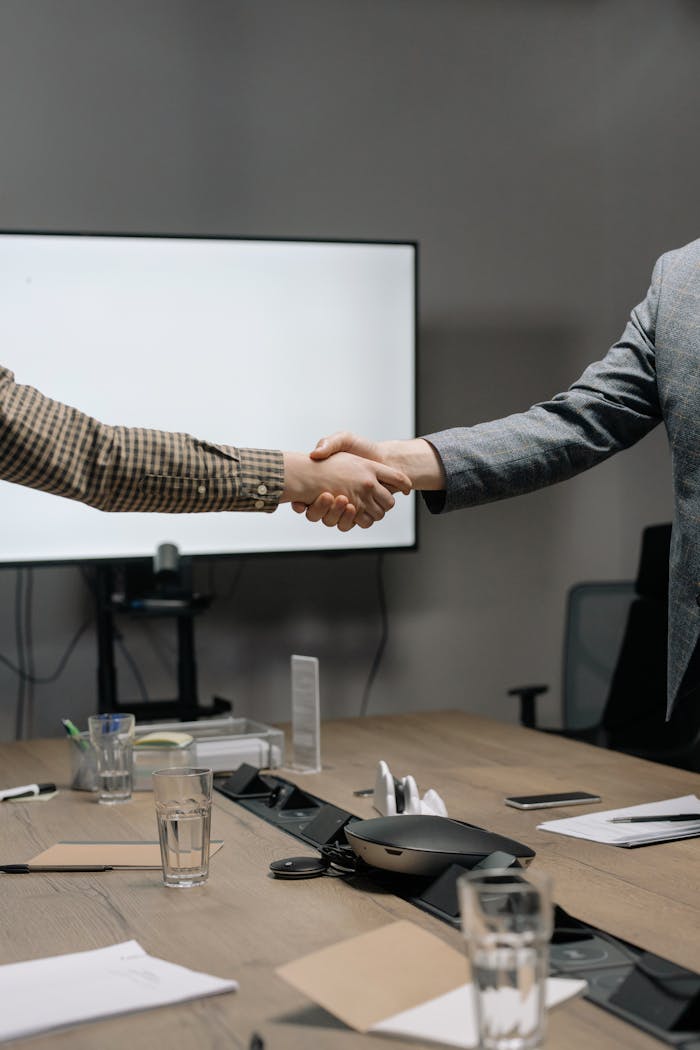 our-experience Two business professionals shaking hands in a modern meeting room, symbolizing successful collaboration.