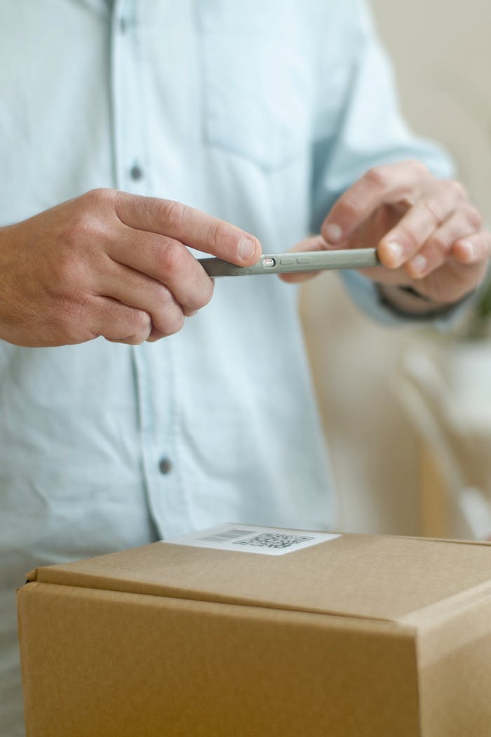 A man using a smartphone to scan a QR code on a package indoors.